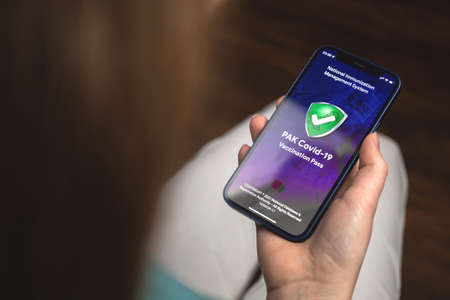 Kharkov, Ukraine - January 10, 2022: Woman uses PAK COVID-19 Vaccination Pass app. Hand with Apple iPhone, mobile phone screen with logoのeditorial素材