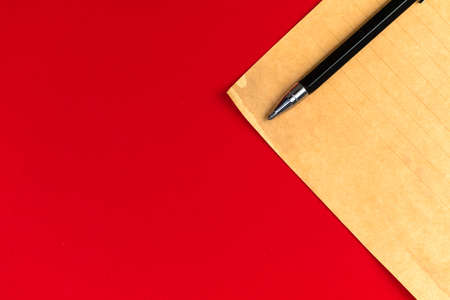 Vintage letter paper with black pencil on a bright red table background with copy space, top view photoの写真素材