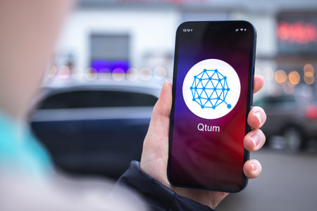 Kharkov, Ukraine - February 2, 2022: Qtum coin symbol. Trade with cryptocurrency, digital and virtual money, mobile banking. Hand with smartphone, screen with crypto icon close-upのeditorial素材