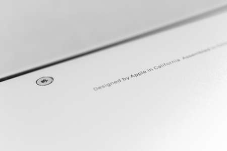 Apple Macbook designed by Apple in California text on laptop bottom close-up view photoのeditorial素材