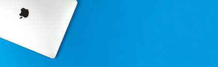 Apple Macbook on bright blue table background, banner with copy space. Business and office concept, top view, flat layのeditorial素材