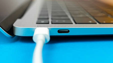 Charging laptop with modern USB Type C port. Laptop low battery concept, technology background, office table top viewの写真素材
