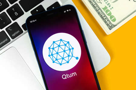 Kharkov, Ukraine - January 31, 2022: Qtum coin symbol. Trade with cryptocurrency, digital and virtual money, banking with mobile phone concept. Business workspace, table with laptop top viewのeditorial素材