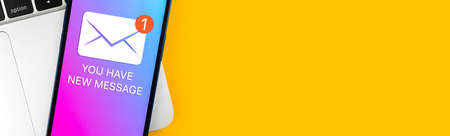 Banner, you have new message text notification on a mobile phone screen close-up view. Business communication concept, laptop and office table backgroundの写真素材