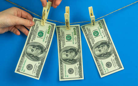 Hands and money laundering. Illegal financial business concept, dollar banknotes hanging on a rope. Corruption and crime, blue background photoの写真素材