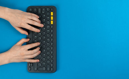 Female hands and keyboard on a blue background. Concept of workspace, work at the home, computer and...