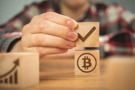 Concept of bitcoin and check mark. BTC symbol on a wooden cubes in hands close-up view. business investment photoの写真素材