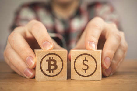 Bitcoin and dollar symbol on a wooden cubes in hands. Concept of cryptocurrency and cash background, wooden tableの写真素材