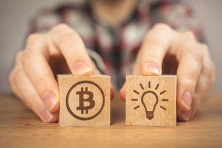 Concept of bitcoin growth. Bulb idea and BTC symbols on a wooden cubes in hands close-up view. business investment photoの写真素材