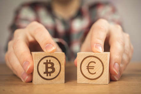 Bitcoin and euro symbol on a wooden cubes in hands. Concept of cryptocurrency and cash background, wooden tableの写真素材