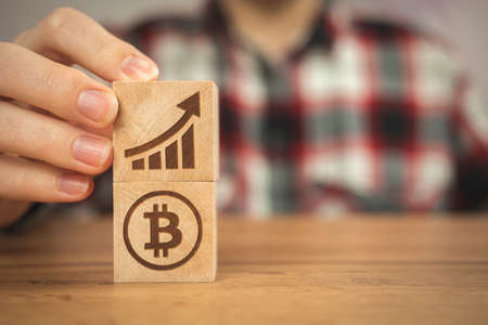 Concept of bitcoin growth. BTC graph of the growth symbols on a wooden cubes in hands close-up view photoの写真素材