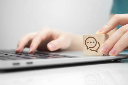 Customer support and IT service assistant. Wooden cube with speech bubble icon and modern laptop close-up view photoの写真素材