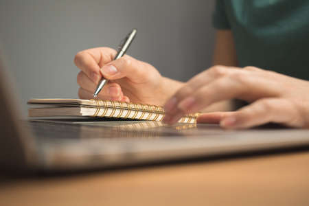 Laptop on wooden desk and young woman hand on keyboard. Freelance workplace, work from home concept backgroundの写真素材
