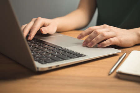 Laptop on wooden desk and young woman hand on keyboard. Freelance workplace, work from home concept backgroundの写真素材