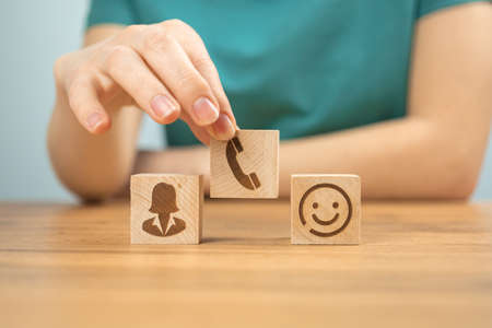 Call center service concept background. Assist, customer service and support. Wooden cubes with icons and young woman hand in office photoの写真素材