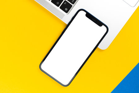 Apple iPhone mockup screen, flat lay office desk with laptop, yellow background. Minimal design, mobile phone mockup, top view, copy spaceのeditorial素材