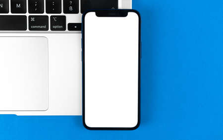 Apple iPhone mockup screen, flat lay office desk with laptop, blue background. Minimal design, mobile phone mockup, top view, copy spaceのeditorial素材