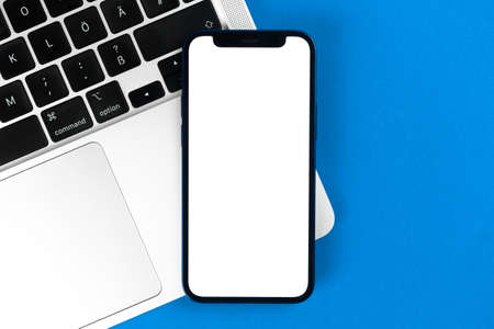 Apple iPhone mockup screen, flat lay office desk with laptop, blue background. Minimal design, mobile phone mockup, top view, copy spaceのeditorial素材