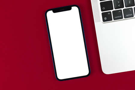 Flat lay Apple iPhone mockup, office desktop with laptop, red burgundy background. Top view, copy space photoのeditorial素材