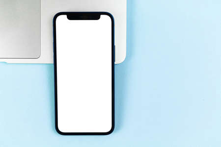 Flat lay Apple iPhone screen mockup, office desktop with laptop, bright blue background. Top view, copy space photoのeditorial素材