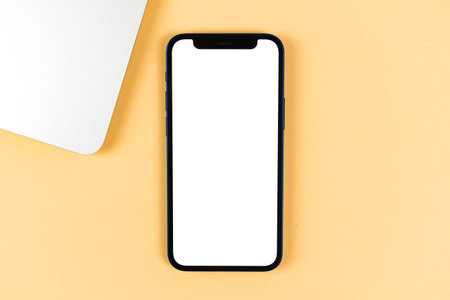 Flat lay Apple iPhone mockup, office desktop with laptop, bright beige background. Top view, copy space photoのeditorial素材