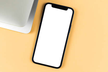 Flat lay Apple iPhone mockup, office desktop with laptop, bright beige background. Top view, copy space photoのeditorial素材