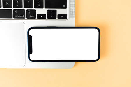 Flat lay Apple iPhone horizontally mockup, office desktop with laptop, beige background. Top view, copy space photoのeditorial素材