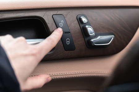 Hand with car door lock switch inside the luxury car interior with leather and wood design. close-up viewの写真素材