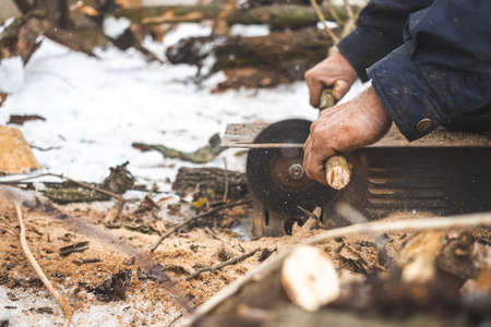 Man cutting wood using stationary circular saw outdoors in winter for kindling close-upの写真素材