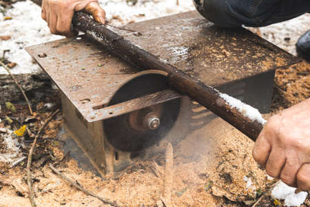 Man cutting wood using stationary circular saw outdoors in winter for kindling close-upの写真素材