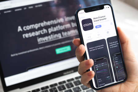 Poltava, Ukraine - April 5, 2022: Atom Finance app icon. Hand with mobile phone with application. Mobile banking and investment conceptのeditorial素材