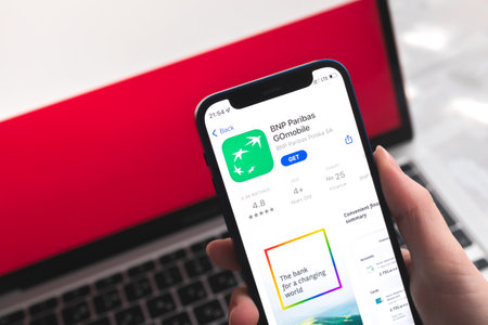 Poltava, Ukraine - April 7, 2022: BNP Paribas mobile banking app in Poland. Hand with smartphone, on the screen. background with national flag photoのeditorial素材