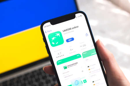 Poltava, Ukraine - April 7, 2022: Ukrsib mobile banking app in Ukraine. Hand with smartphone, on the screen. background with national flag photoのeditorial素材
