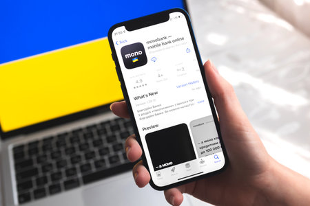 Poltava, Ukraine - April 7, 2022: Monobank mobile banking app in Ukraine. Hand with smartphone, on the screen. background with national flag photoのeditorial素材
