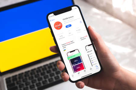Poltava, Ukraine - April 7, 2022: PUMB mobile banking app in Ukraine. Hand with smartphone,  on the screen. background with national flag photoのeditorial素材