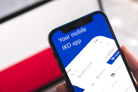 Poltava, Ukraine - April 7, 2022: IKO mobile banking app in Poland. Hand with smartphone, on the screen. background with national flag photoのeditorial素材