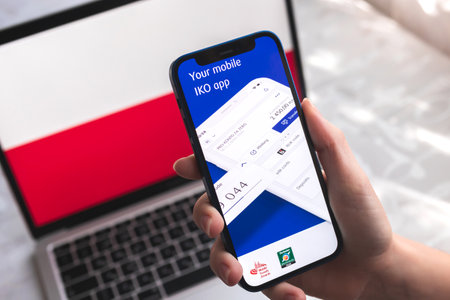 Poltava, Ukraine - April 7, 2022: IKO mobile banking app in Poland. Hand with smartphone, on the screen. background with national flag photoのeditorial素材