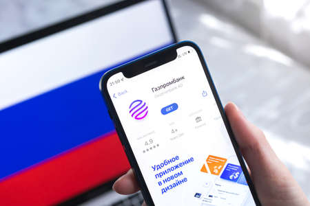 SPB, Russia - April 7, 2022: Gazprombank mobile banking app in Russia. Hand with smartphone, icon on the screen. background with national flag photoのeditorial素材