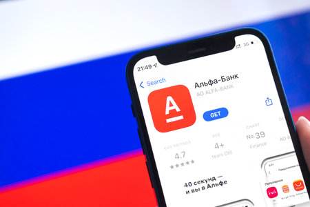 SPB, Russia - April 7, 2022: AlfaBank mobile banking app in Russia. Hand with smartphone, icon on the screen. background with national flag photoのeditorial素材