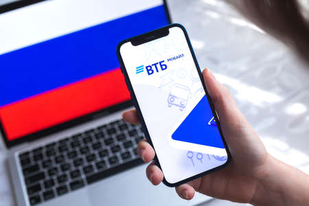 SPB, Russia - April 7, 2022: VTB mobile banking app in Russia. Hand with smartphone, on the screen. background with national flag photoのeditorial素材