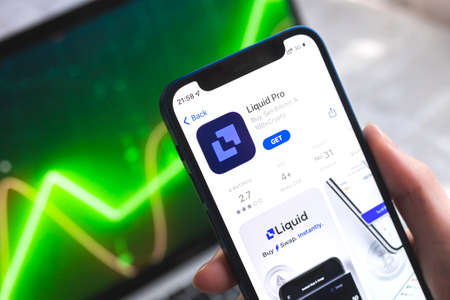 Poltava, Ukraine - April 7, 2022: Liquid Pro crypto currency wallet app. Hand with smartphone, on the screen. stock chart backgroundのeditorial素材