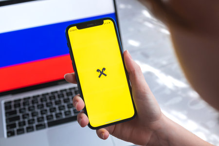SPB, Russia - April 7, 2022: Raiffeisen mobile banking app in Russia. Hand with smartphone,  on the screen. background with national flag photoのeditorial素材