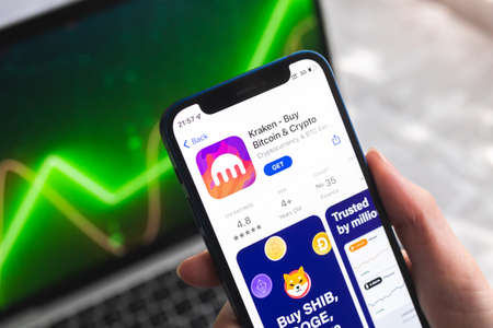 Poltava, Ukraine - April 7, 2022: Kraken crypto currency wallet app. Hand with smartphone, on the screen. stock chart backgroundのeditorial素材