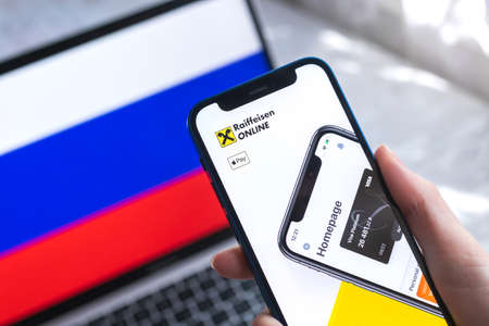 SPB, Russia - April 7, 2022: Raiffeisen mobile banking app in Russia. Hand with smartphone,  on the screen. background with national flag photoのeditorial素材