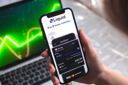 Poltava, Ukraine - April 7, 2022: Liquid Pro crypto currency wallet app. Hand with smartphone, on the screen. stock chart backgroundのeditorial素材