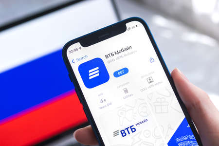 SPB, Russia - April 7, 2022: VTB mobile banking app in Russia. Hand with smartphone, icon on the screen. background with national flag photoのeditorial素材