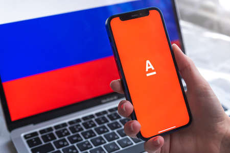 SPB, Russia - April 7, 2022: AlfaBank mobile banking app in Russia. Hand with smartphone, on the screen. background with national flag photoのeditorial素材