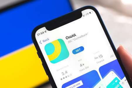 Poltava, Ukraine - April 7, 2022: Oschadbank mobile banking app in Ukraine. Hand with smartphone, on the screen. background with national flag photoのeditorial素材