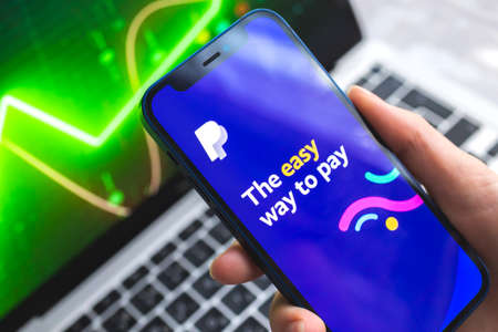Poltava, Ukraine - April 7, 2022: Paypal mobile banking app. Hand with smartphone, on the screen. stock chart backgroundのeditorial素材