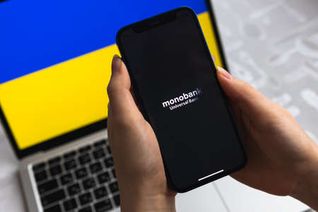Poltava, Ukraine - April 8, 2022: Monobank in Ukraine. Mobile banking app for Ukraine users. Flag background, mobile phone with icon close-up view photoのeditorial素材